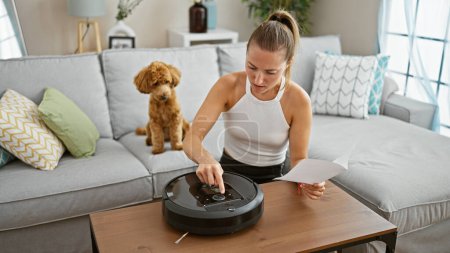 Foto de Joven mujer caucásica con instrucciones de lectura de perros iniciando robot aspiradora en casa - Imagen libre de derechos