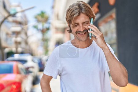 Téléchargez les photos : Jeune homme blond souriant confiant parler sur le smartphone à la rue - en image libre de droit