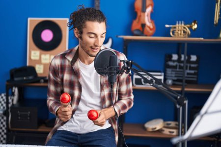 Téléchargez les photos : Jeune homme hispanique musicien chantant une chanson jouant des maracas au studio de musique - en image libre de droit