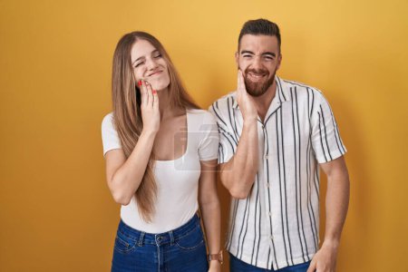 Photo for Young couple standing over yellow background touching mouth with hand with painful expression because of toothache or dental illness on teeth. dentist - Royalty Free Image