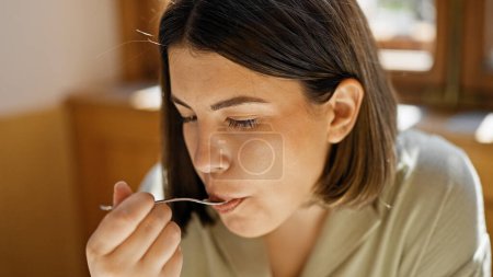 Photo for Young beautiful hispanic woman eating food with fork at cafeteria - Royalty Free Image