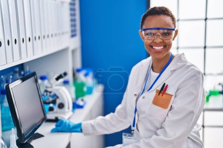 Foto de Científica afroamericana sonriendo confiada usando computadora en laboratorio - Imagen libre de derechos