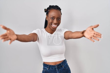 Téléchargez les photos : Belle femme noire debout sur fond isolé regardant la caméra souriant à bras ouverts pour se faire câliner. expression joyeuse embrassant le bonheur. - en image libre de droit