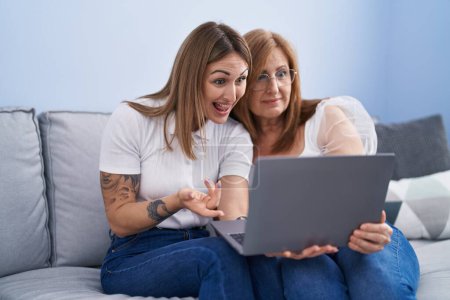 Téléchargez les photos : Mère et fille utilisant un ordinateur portable assis sur le canapé à la maison - en image libre de droit