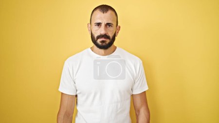 Photo for Young hispanic man standing with serious expression over isolated yellow background - Royalty Free Image