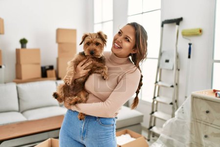 Téléchargez les photos : Jeune belle femme hispanique souriant chien câlin confiant à la nouvelle maison - en image libre de droit
