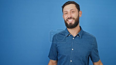 Foto de Joven hombre hispano sonriendo confiado de pie sobre aislado fondo azul - Imagen libre de derechos