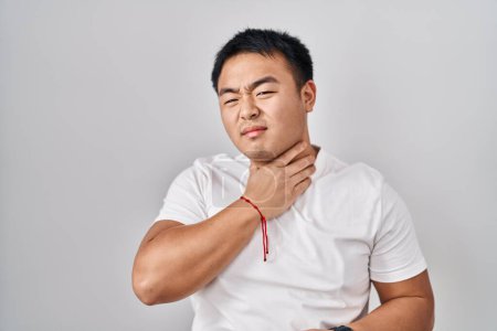 Téléchargez les photos : Jeune homme chinois debout sur fond blanc touchant cou douloureux, mal de gorge pour la grippe, la motte et l'infection - en image libre de droit