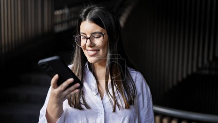 Photo for Young beautiful hispanic woman smiling happy using smartphone at the office - Royalty Free Image