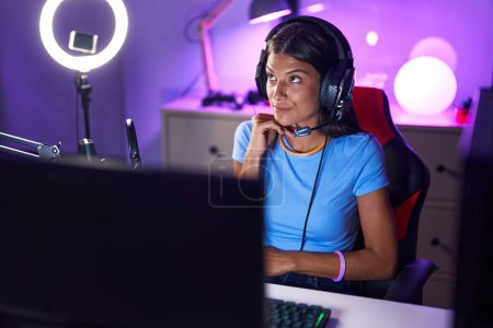 Photo for Brunette young woman playing video games serious face thinking about question with hand on chin, thoughtful about confusing idea - Royalty Free Image