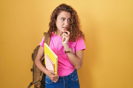 Photo for Young caucasian woman wearing student backpack and holding books thinking worried about a question, concerned and nervous with hand on chin - Royalty Free Image