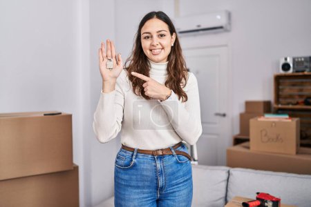 Téléchargez les photos : Young hispanic woman holding keys of new home smiling happy pointing with hand and finger - en image libre de droit