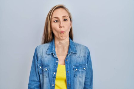 Photo for Young blonde woman standing over blue background making fish face with lips, crazy and comical gesture. funny expression. - Royalty Free Image