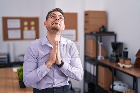 Photo for Young hispanic man at the office begging and praying with hands together with hope expression on face very emotional and worried. begging. - Royalty Free Image