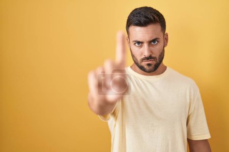 Téléchargez les photos : Bel homme hispanique debout sur fond jaune pointant du doigt et l'expression en colère, ne montrant aucun geste - en image libre de droit
