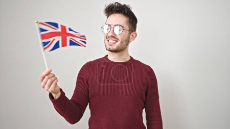 Téléchargez les photos : Jeune homme hispanique souriant confiant tenant drapeau du royaume uni sur fond blanc isolé - en image libre de droit