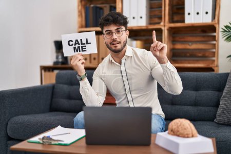 Photo for Hispanic man with beard working at therapy office holding call me sign surprised with an idea or question pointing finger with happy face, number one - Royalty Free Image