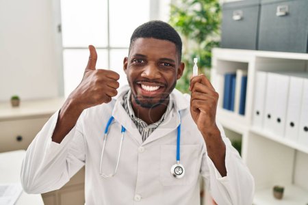 Photo for African american doctor man holding eye drops smiling happy and positive, thumb up doing excellent and approval sign - Royalty Free Image