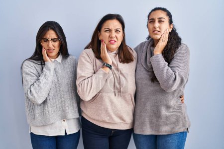 Photo for Mother and two daughters standing over blue background touching mouth with hand with painful expression because of toothache or dental illness on teeth. dentist concept. - Royalty Free Image