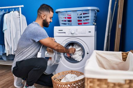 Foto de Joven hombre hispano sonriendo confiado lavando ropa en la lavandería - Imagen libre de derechos