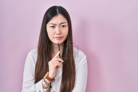 Photo for Chinese young woman holding pencil over pink background skeptic and nervous, frowning upset because of problem. negative person. - Royalty Free Image