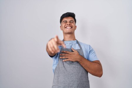 Photo for Hispanic young man wearing apron over white background laughing at you, pointing finger to the camera with hand over body, shame expression - Royalty Free Image