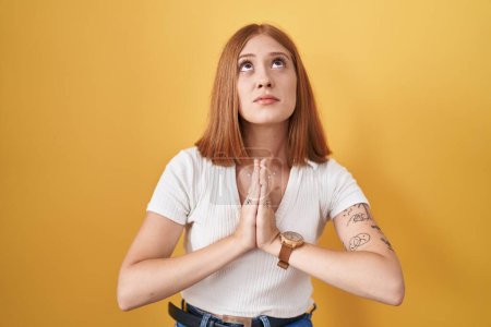 Photo for Young redhead woman standing over yellow background begging and praying with hands together with hope expression on face very emotional and worried. begging. - Royalty Free Image