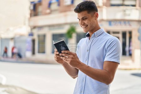 Téléchargez les photos : Jeune homme hispanique souriant lecture confiante passeport canadien à la rue - en image libre de droit