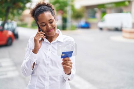 Téléchargez les photos : Femme afro-américaine parlant sur smartphone tenant une carte de crédit à la rue - en image libre de droit