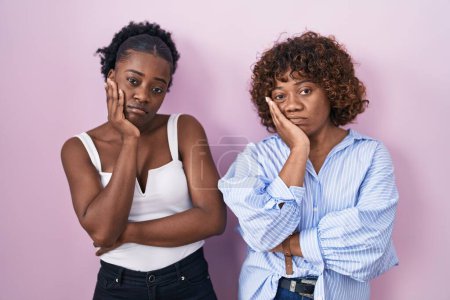 Téléchargez les photos : Deux femmes africaines debout sur fond rose pensant fatigué et ennuyé avec des problèmes de dépression avec les bras croisés. - en image libre de droit