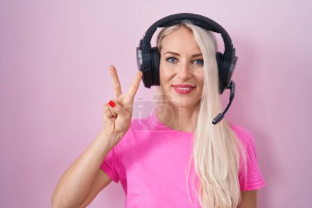 Téléchargez les photos : Femme caucasienne écoutant de la musique à l'aide d'écouteurs montrant et pointant vers le haut avec les doigts numéro deux tout en souriant confiant et heureux. - en image libre de droit