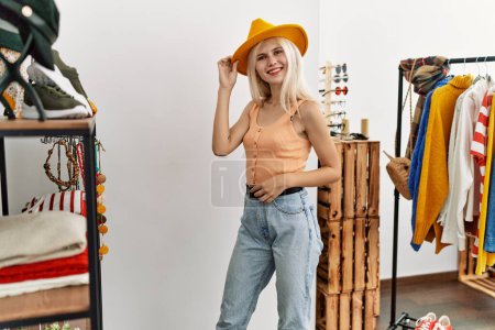 Téléchargez les photos : Jeune femme blonde cliente portant un chapeau souriant au magasin de vêtements - en image libre de droit