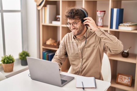 Téléchargez les photos : Jeune homme d'affaires utilisant un ordinateur portable et des écouteurs travaillant au bureau - en image libre de droit