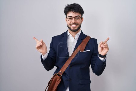 Foto de Hombre hispano con barba vistiendo ropa de negocios sonriendo confiado señalando con los dedos a diferentes direcciones. espacio de copia para publicidad - Imagen libre de derechos