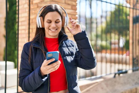 Téléchargez les photos : Jeune belle femme hispanique souriant confiant écouter de la musique dans la rue - en image libre de droit