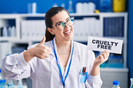 Photo for Young brunette woman working on cruelty free laboratory smiling happy and positive, thumb up doing excellent and approval sign - Royalty Free Image