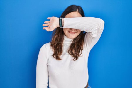 Photo for Young hispanic woman standing over blue background covering eyes with arm, looking serious and sad. sightless, hiding and rejection concept - Royalty Free Image