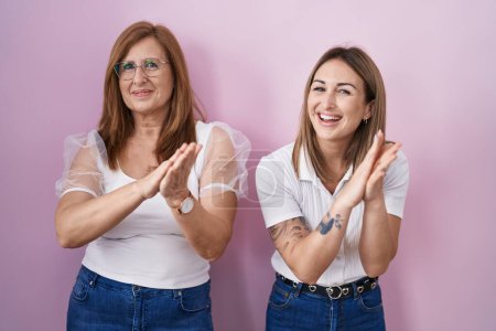 Téléchargez les photos : Mère et fille hispaniques portant t-shirt blanc décontracté sur fond rose applaudissements heureux et joyeux, souriant mains fières ensemble - en image libre de droit
