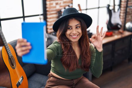 Photo for Hispanic young woman doing video call with tablet doing ok sign with fingers, smiling friendly gesturing excellent symbol - Royalty Free Image