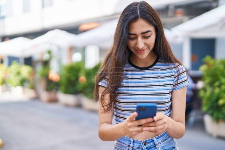 Photo for Young hispanic girl smiling confident using smartphone at street - Royalty Free Image