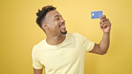 Téléchargez les photos : Afro-Américain tenant une carte de crédit souriant sur fond jaune isolé - en image libre de droit