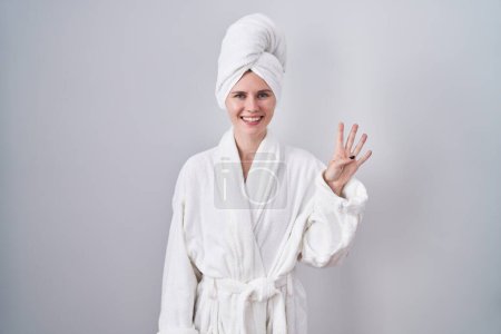 Photo for Blonde caucasian woman wearing bathrobe showing and pointing up with fingers number four while smiling confident and happy. - Royalty Free Image