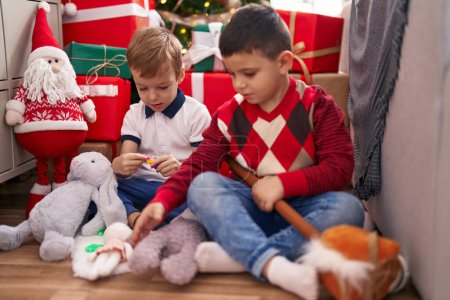 Téléchargez les photos : Deux enfants jouent avec des jouets assis sur le sol près de l'arbre de Noël à la maison - en image libre de droit