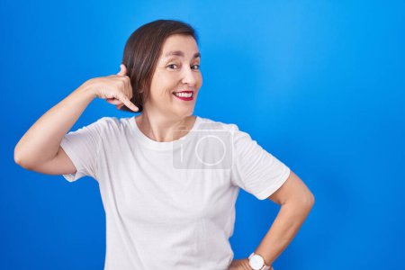 Photo for Middle age hispanic woman standing over blue background smiling doing phone gesture with hand and fingers like talking on the telephone. communicating concepts. - Royalty Free Image