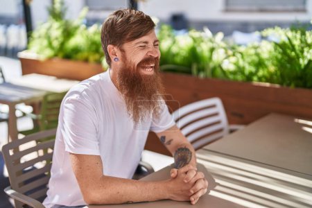 Photo for Young redhead man smiling confident sitting on table at coffee shop terrace - Royalty Free Image