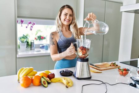 Foto de Young woman smiling confident pouring water on blender at kitchen - Imagen libre de derechos