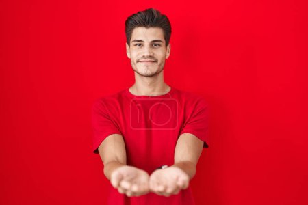 Photo for Young hispanic man standing over red background smiling with hands palms together receiving or giving gesture. hold and protection - Royalty Free Image