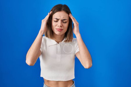 Photo for Hispanic woman standing over blue background with hand on head for pain in head because stress. suffering migraine. - Royalty Free Image