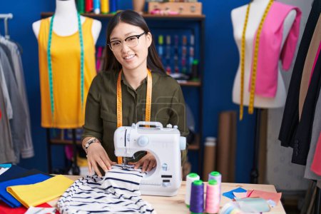 Foto de Mujer china sastre sonriendo confiado usando máquina de coser en el estudio de costura - Imagen libre de derechos