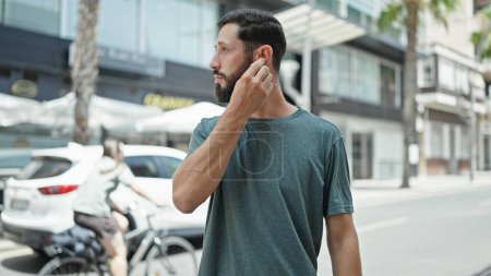 Téléchargez les photos : Jeune homme hispanique écoutant de la musique regardant du côté de la rue - en image libre de droit